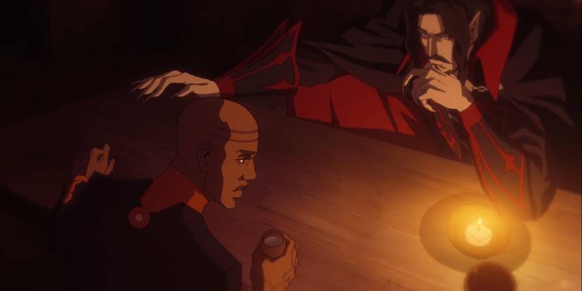 Dracula and Isaac talking at a table.