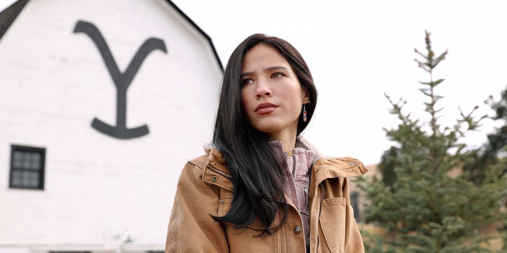 Monica Long Dutton (Kelsey Asbille) stands in front of a barn while looking serious in Yellowstone.