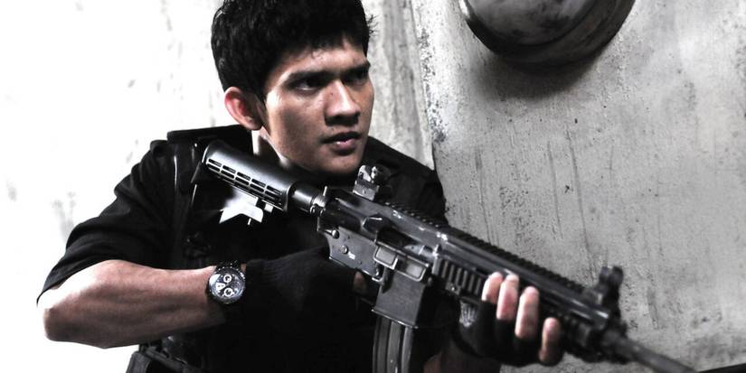 Rama (Iko Uwais) is holding a gun while rounding a corner in The Raid: Redemption.