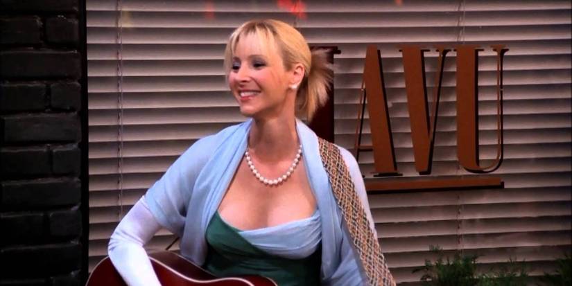 Phoebe Buffay smiles while holding her guitar outside a storefront in Friends.