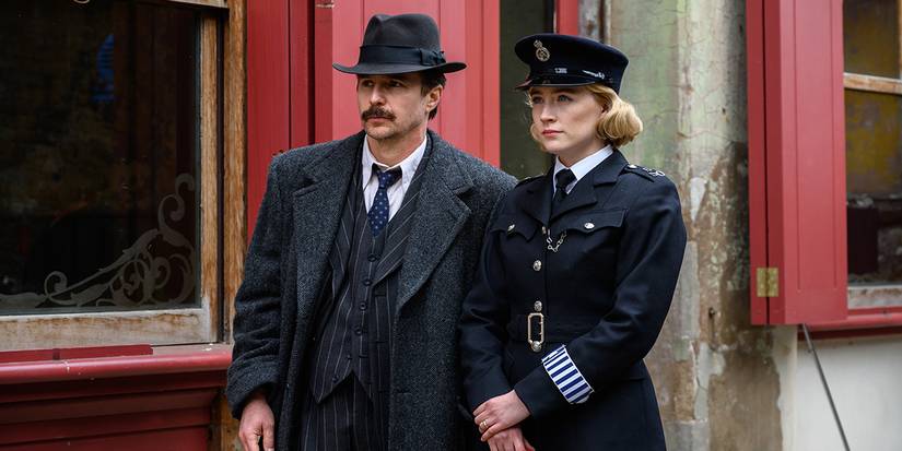 Sam Rockwell and Saoirse Ronan in See How They Run standing against a wall.