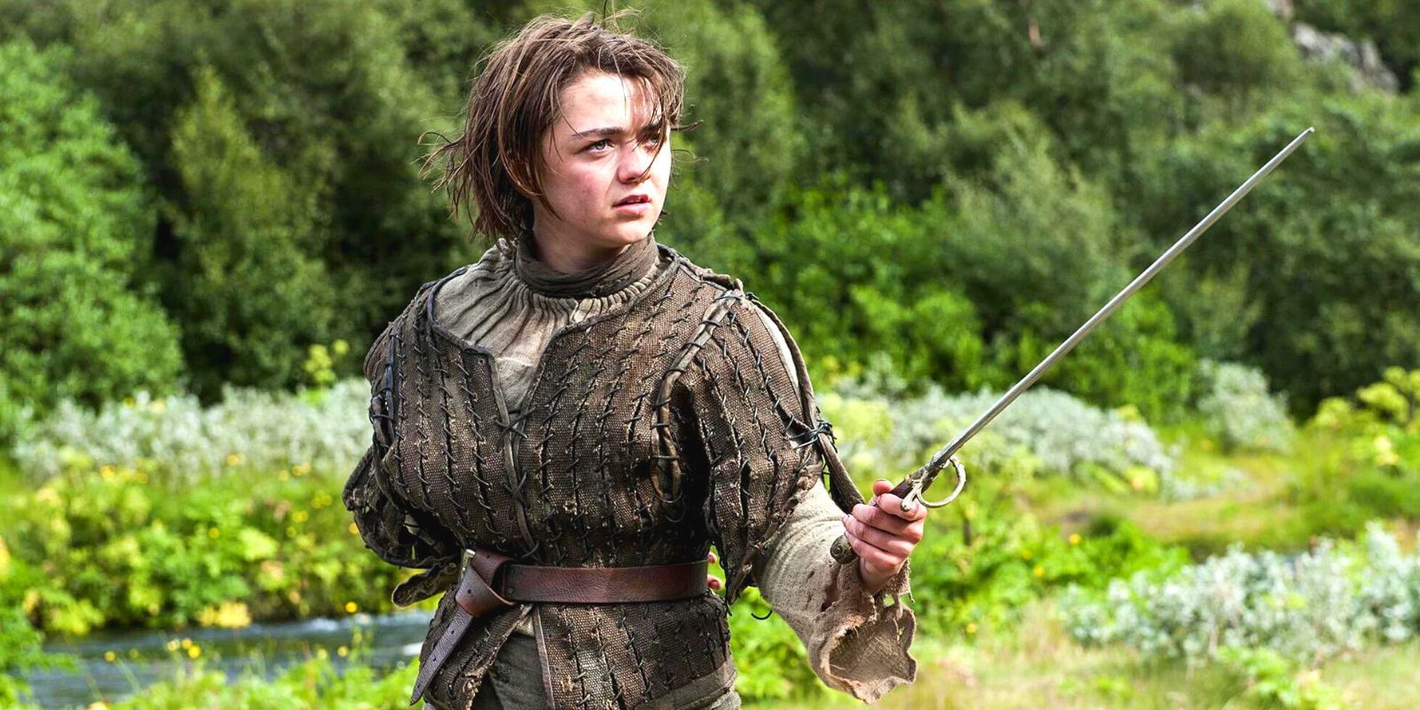 Arya Stark (Maisie Williams) segurando sua espada pronta em um campo verde em Game of Thrones.