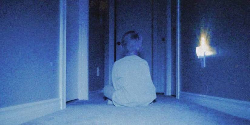 Kevin sits on the floor facing away from camera in the dark next to a nightlight in Skinamarink.