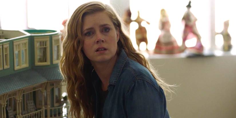 Camille is standing near the dollhouse in Sharp Objects.