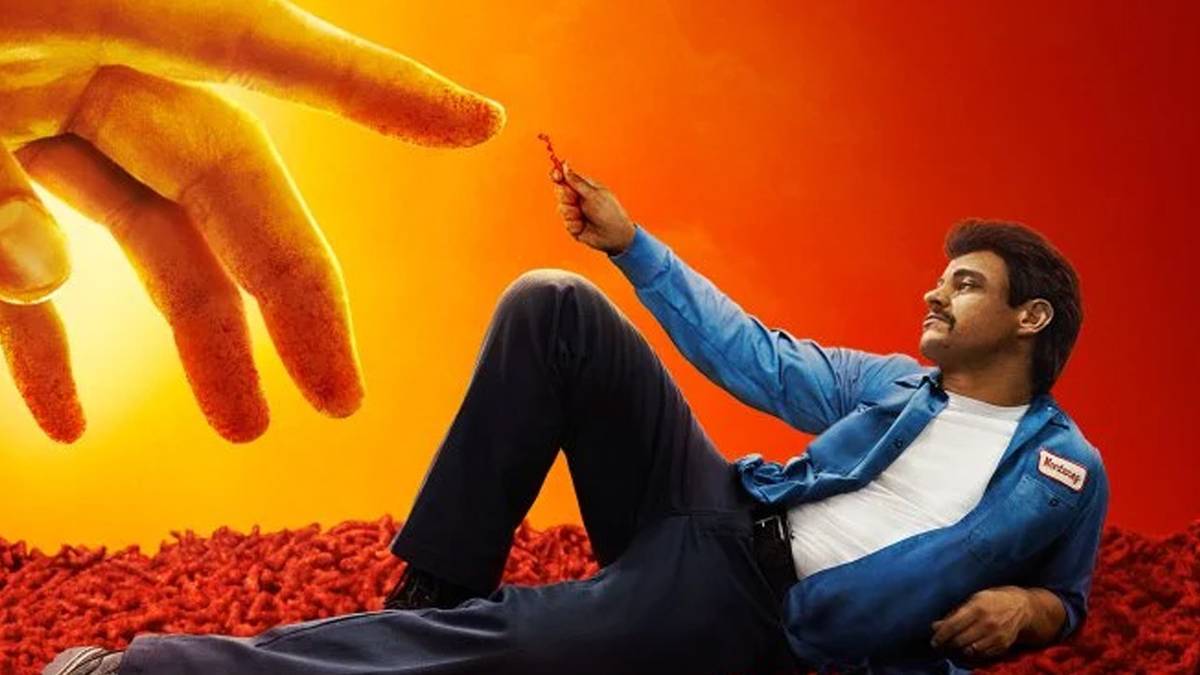 Richard Montañez holds a Flamin' Hot Cheeto up to a Cheeto dust-covered finger.