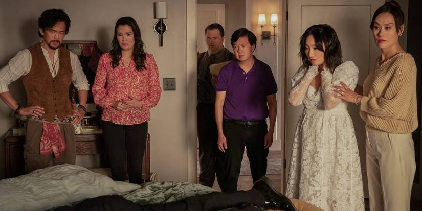 Several people stand around a dead body on a bed in a scene from The Afterparty.