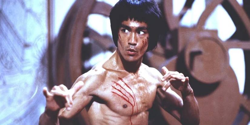 Lee (Bruce Lee) has scratches on his face and chest as he faces off against enemies in Enter the Dragon.