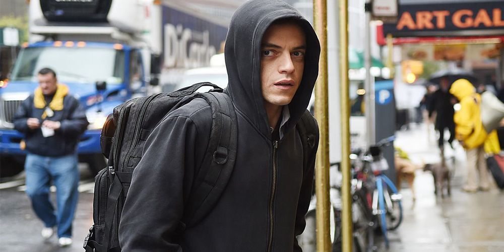 Rami Malek as Elliot Anderson standing in the street with a backpack and hoodie in Mr. Robot