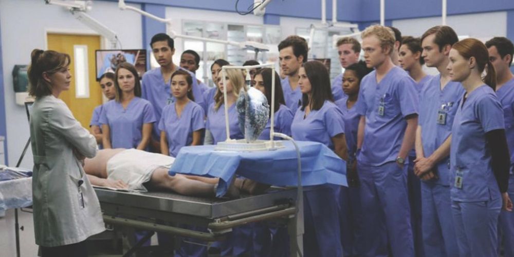 Ellen Pompeo as Meredith Grey teaches a large group of interns in blue scrubs on Grey's Anatomy