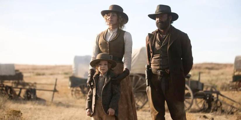 James and Margaret Dutton stand outside amidst the wagon train with their son, John in 1883.