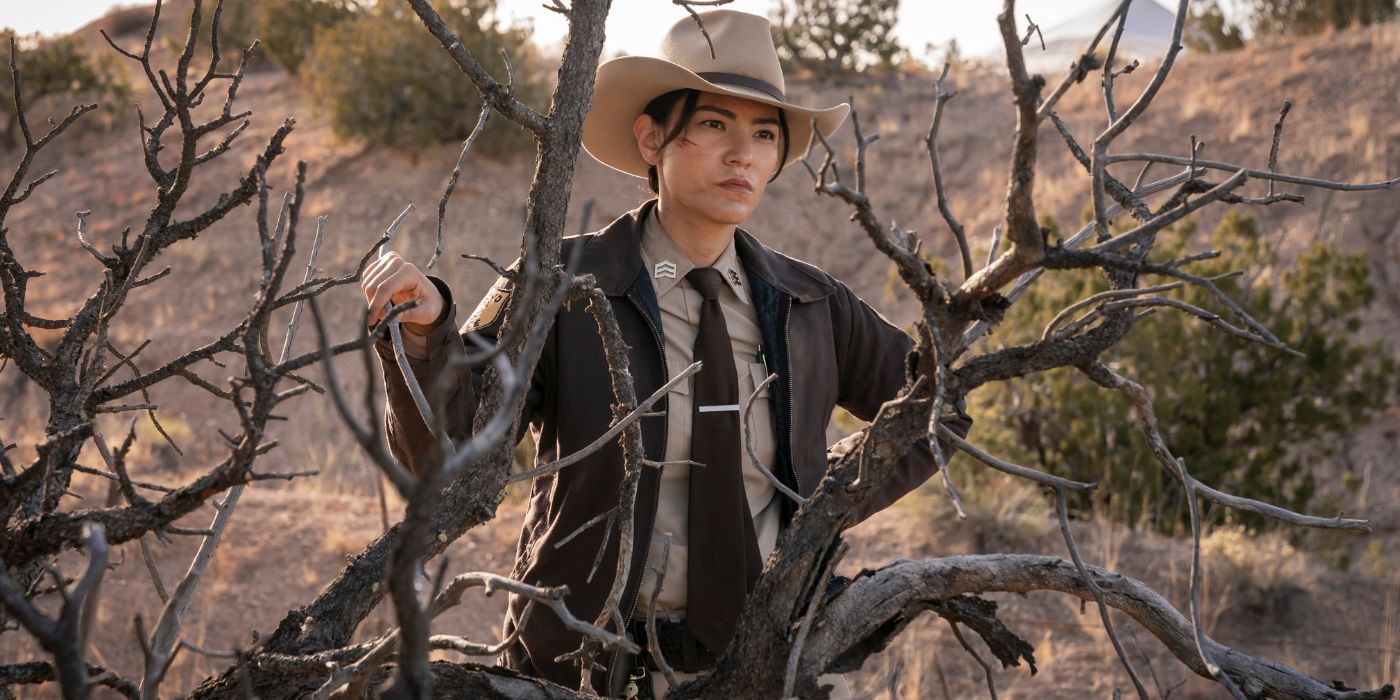 Bernadette from Dark Winds stands behind a dead tree outside in the desert.