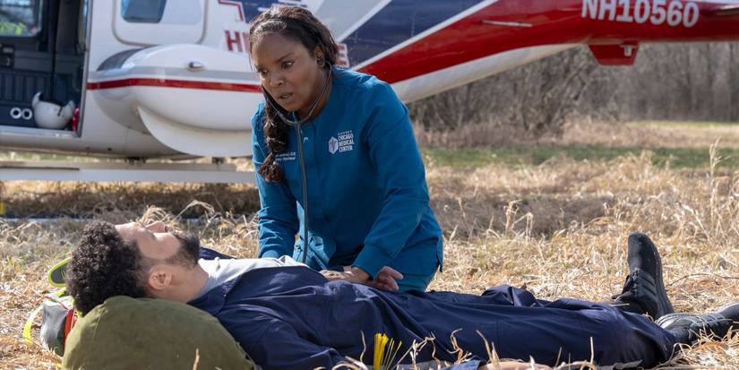 Maggie kneels next to a prone Loren in a field after the emergency landing on Chicago Med.