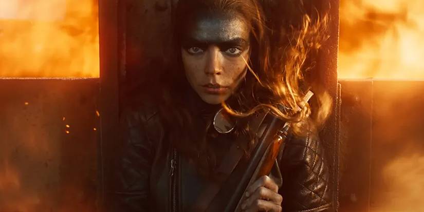 Furiosa holds her shotgun while standing in front of flames in Furiosa A Mad Max Saga.