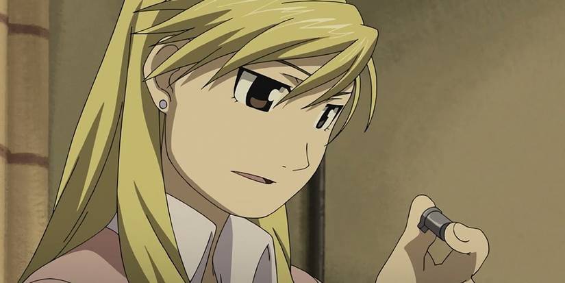 Riza Hawkeye talks as she holds a metal item in her fingers.