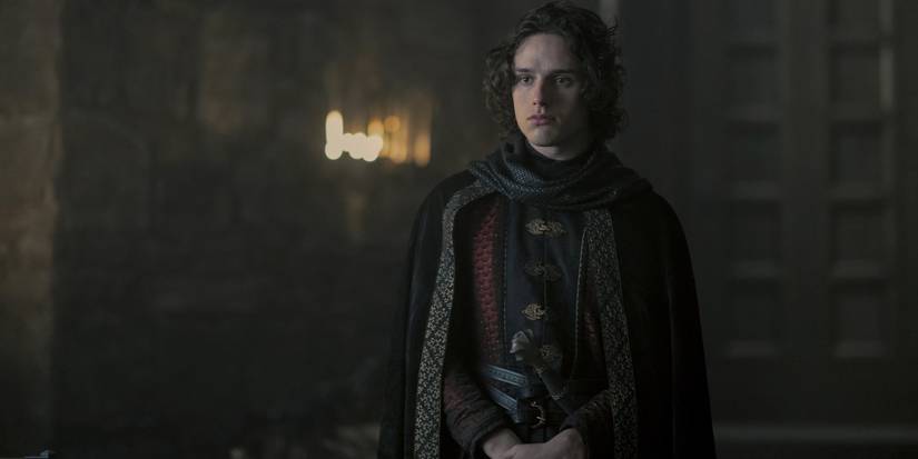 Harry Collett standing in a hall wearing all black as Jacaerys Velaryon on House of the Dragon