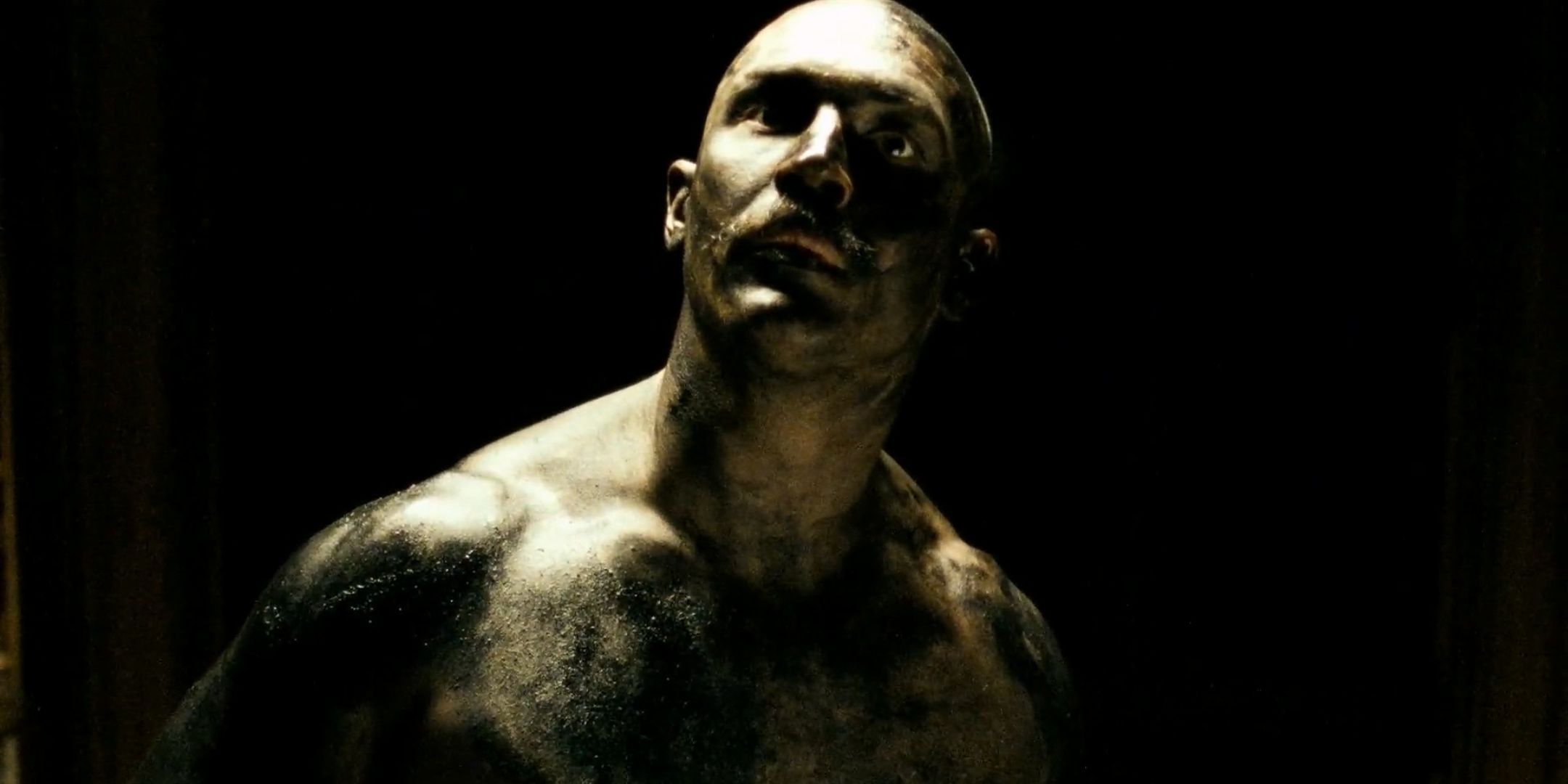 Tom Hardy as Charlie Bronson covered in black paint looks up in Bronson