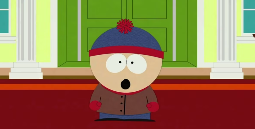 Cartman stands in front of a building with his mouth open in surprise.