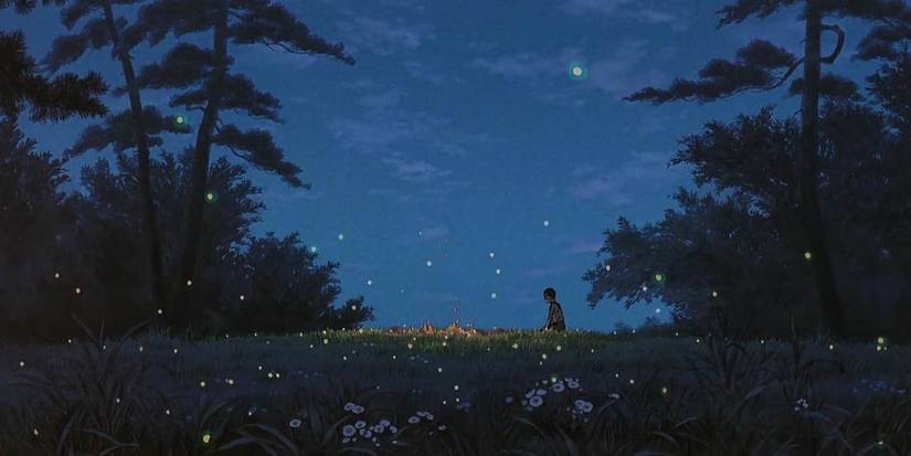 Seita sits and watches the embers of his sister's cremation pyre at night as fireflies fly in Grave of the Fireflies