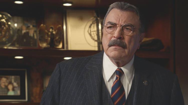Frank Reagan, played by Tom Selleck, sits behind his desk in a suit in Blue Bloods Season 14