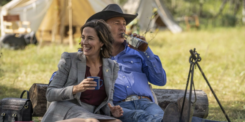 Lynelle Perry (Wendy Moniz) and John Dutton (Kevin Costner) are drinking together on a blanket outside in Yellowstone.