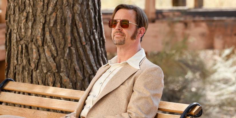 Timothy McGee (Sean Murray) sits on a bench in a tan 1970s suit with sideburns and glasses in NCIS
