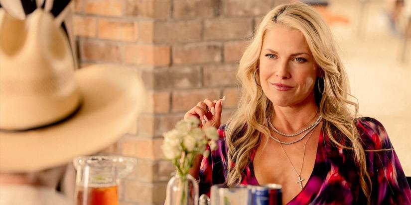Angela, played by Ali Larter, wearing a pink print dress staring across a table at Tommy in Landman