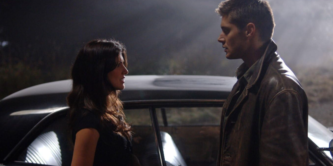 Dean conversa com uma mulher ao lado de um carro à noite em Supernatural.