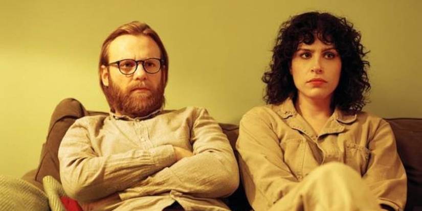 Two characters sit on a couch in The Bisexual.