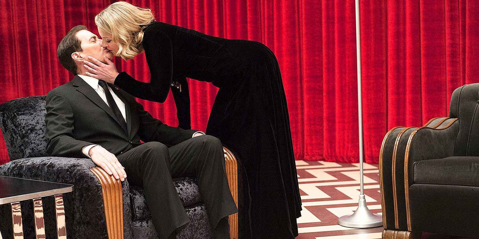 Dale Cooper sitting in a black chair while Laura Palmer in a black dress leans over and kisses him in Black Lodge Twin Peaks the Return