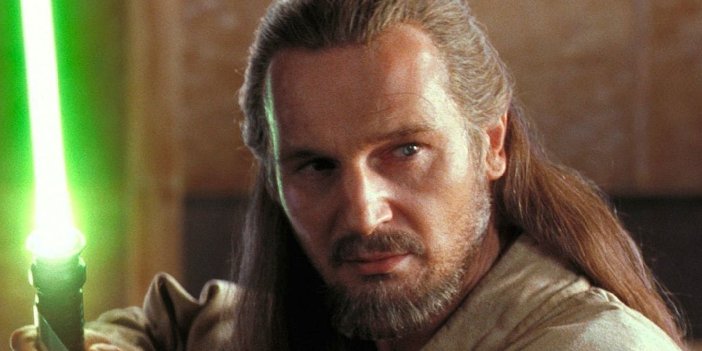 Liam Neeson as Qui-Gon Jinn holds his lightsaber ready in Star Wars.