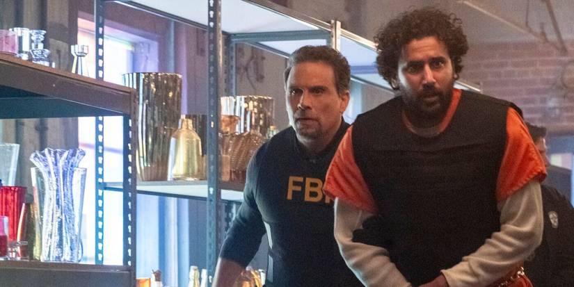 Jubal, wearing an FBI vest, escorts a prisoner in an orange jumpsuit through a store in FBI