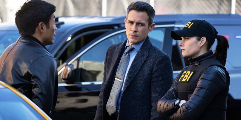 Scola, wearing a black suit, and Maggie, wearing a black FBI vest and cap, speak to a suspect in FBI