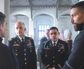 OA looks at Scola, both wearing FBI gear, as they stand in front of two military officers in FBI