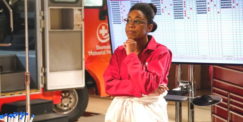 Kasie Hines wearing a red blouse, in front of a computer monitor, next to a bloodmobile, in NCIS