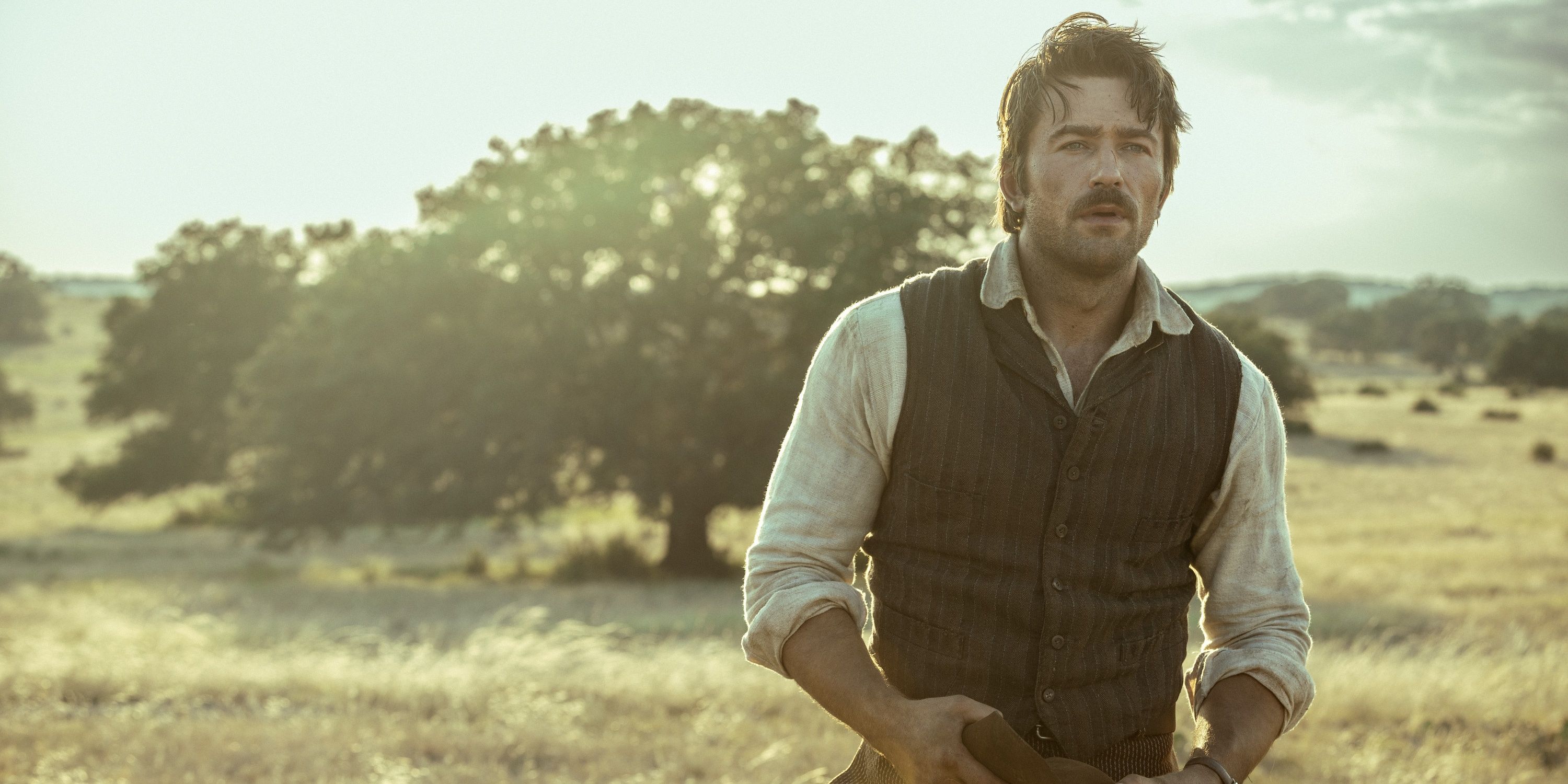 Spencer Dutton wearing a brown vest over a white shirt, standing in a field in the TV show 1923
