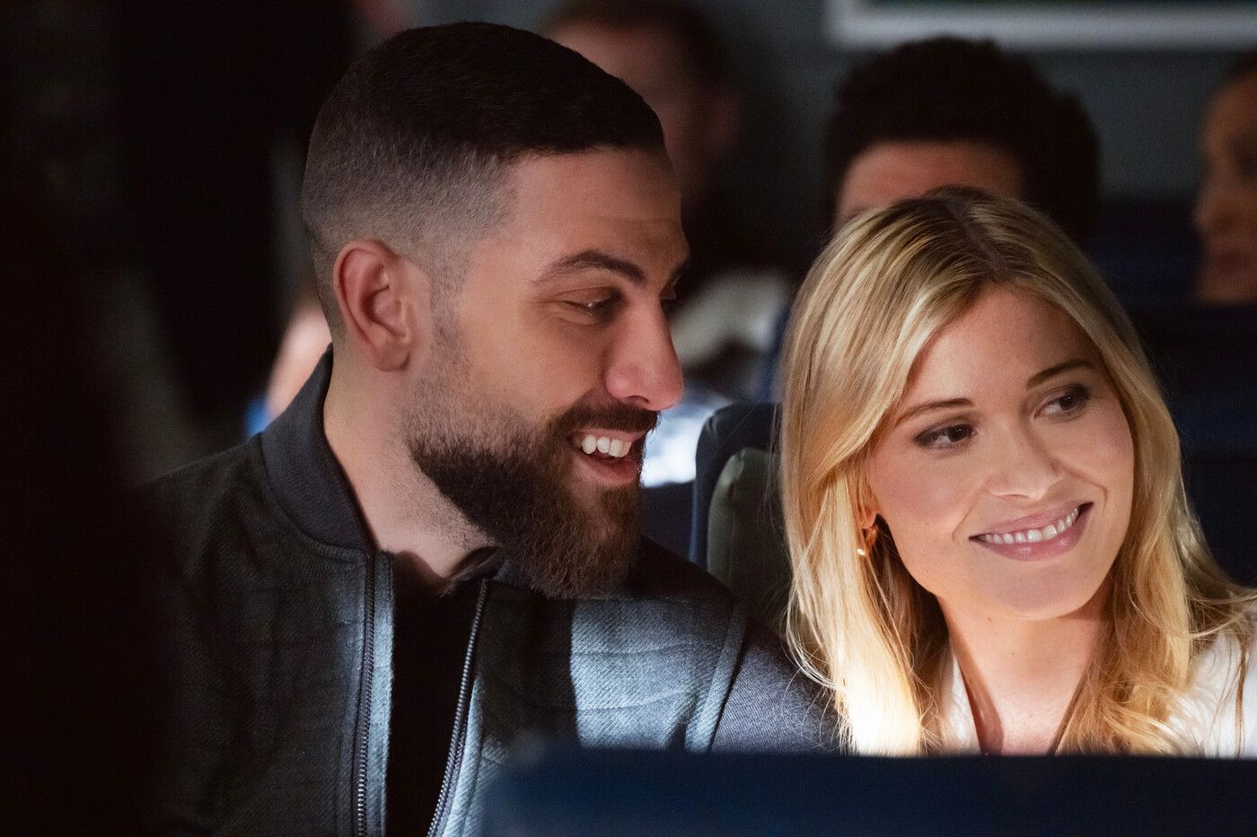 OA Zidan, wearing a black jacket, and Gemma Brooks in a white blouse smile sitting on a train in FBI