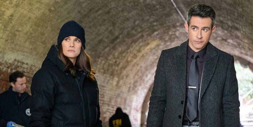 Maggie, wearing a black coat, and Scola, in a black coat and grey suit, stand under a bridge in FBI