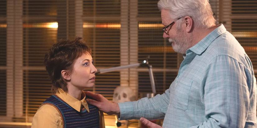 Blue, in a yellow shirt and sweater vest, looks up at Doc Roy, wearing blue shirt, in NCIS: Sydney