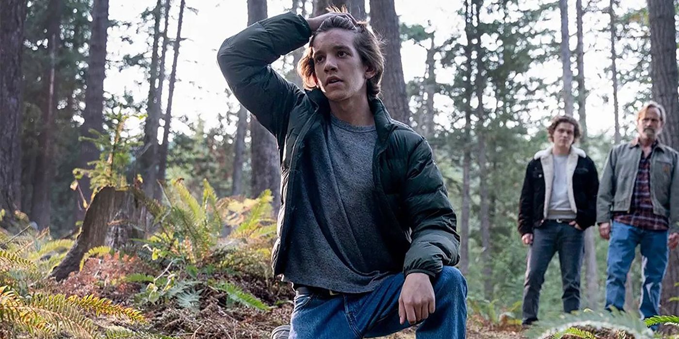 A young Colter kneeling on the ground in the forest, hand slicking his hair back as Russell and Ashton look on in Tracker.
