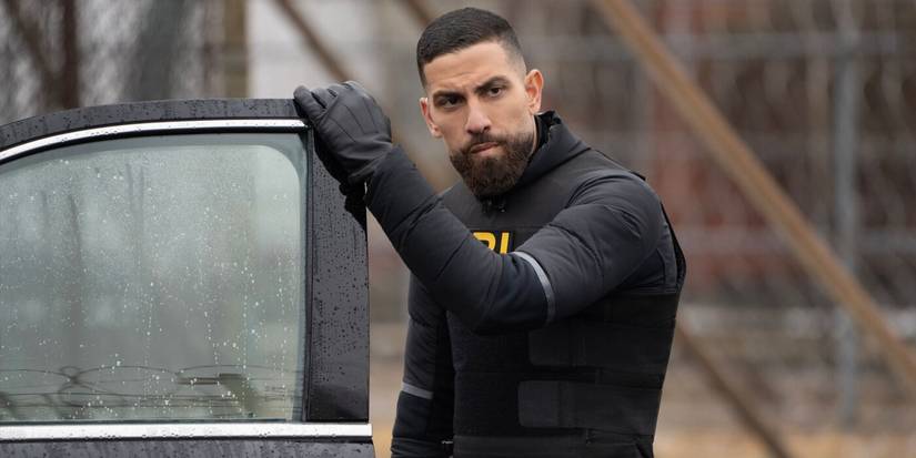 OA, wearing FBI tactical gear, stands next to the open door of a black sedan in the TV show FBI