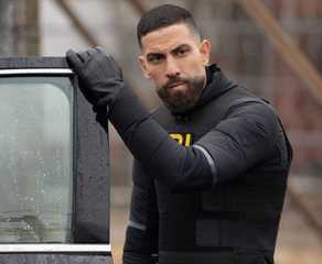 OA, wearing FBI tactical gear, stands next to the open door of a black sedan in the TV show FBI