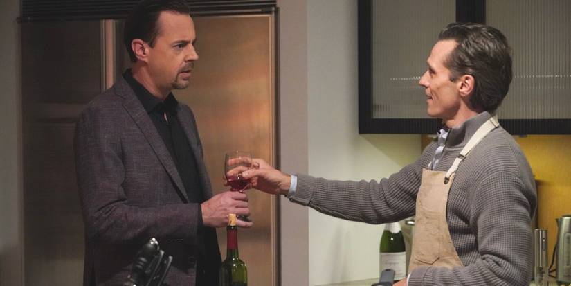 Gabriel Laroche wearing an apron and gesturing toward Timothy McGee in a brown suit on NCIS TV show