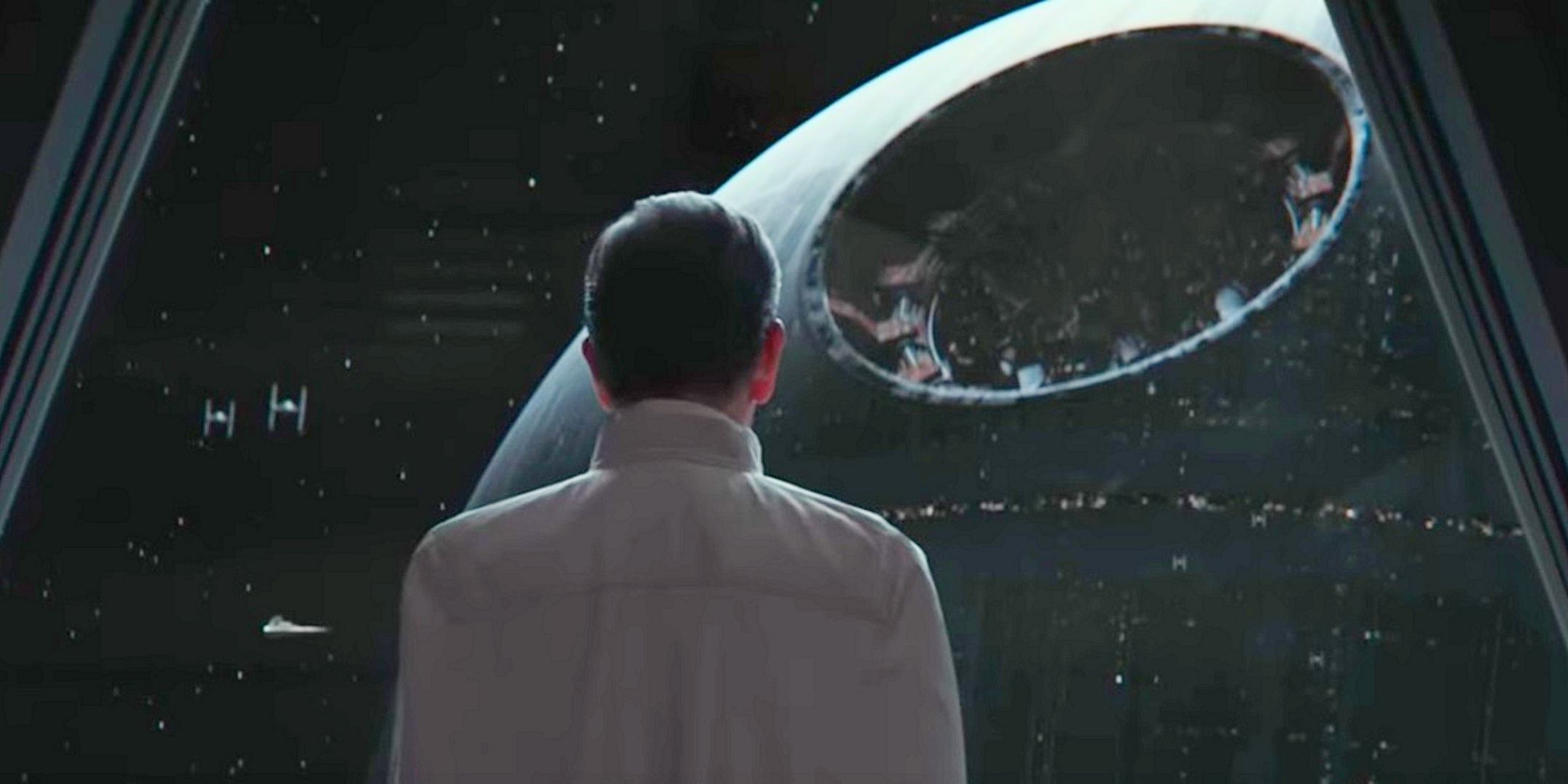 Director Krennic, back to camera, looking out a window at the Death Star without its reflectorr dish from Andor Star Wars