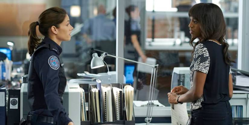Andy wearing a police uniform, standing in the squad room facing Traci in the TV show Rookie Blue