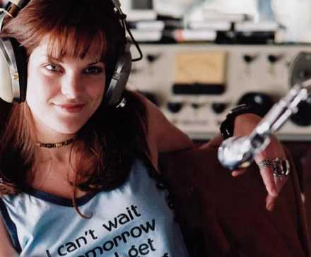 A woman wearing headphones in a radio booth, smiling