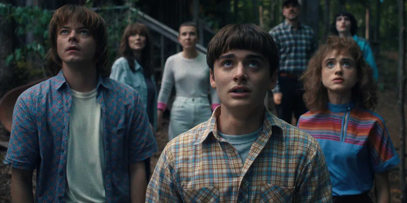 Jonathan, Will and Nancy stand at the front of a group of people looking skyward on Stranger Things