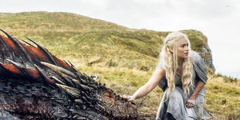 Daenerys Targaryen bends down and pats her dragon.