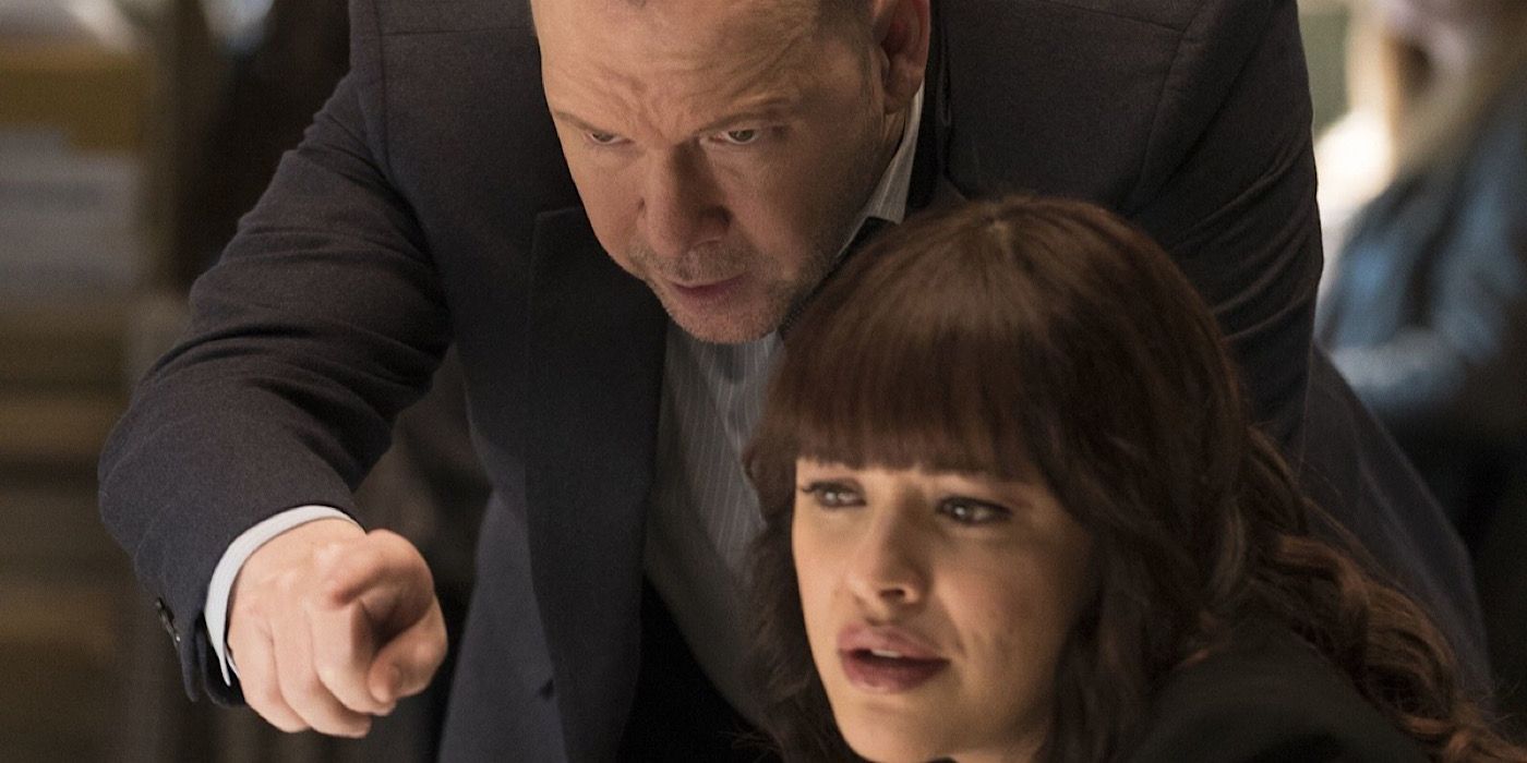 Danny stands over Maria's shoulder and points at the computer screen in front of them.