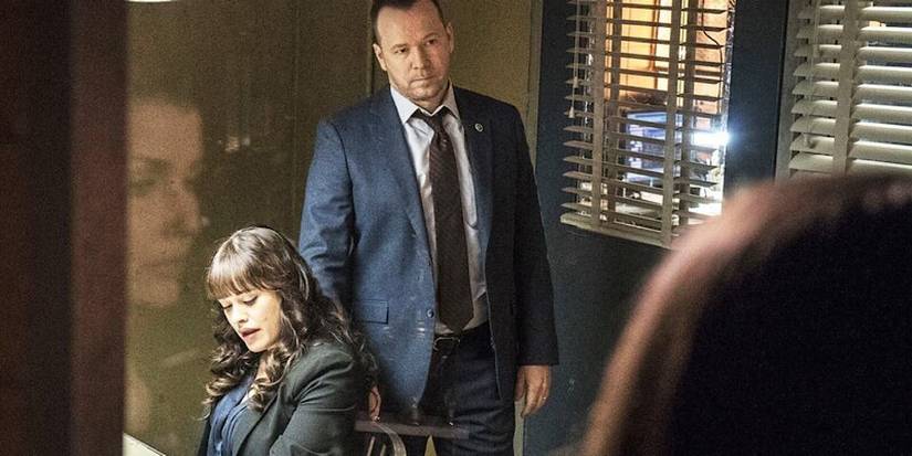 A police officer looks into the interrogation room where Danny stands behind Maria.