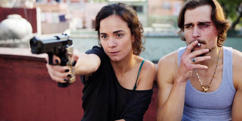 Teresa points a gun at someone of screen as she sits beside James who is smoking a cigarette and has a black eye.